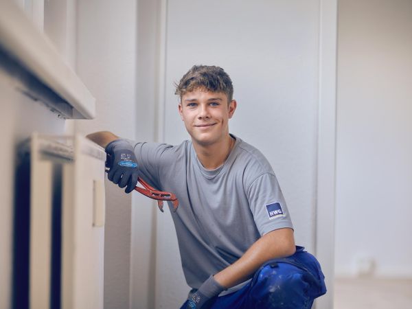 Junger Handwerkerazubi an der Heizung. Eine Rohrzange in der Hand.